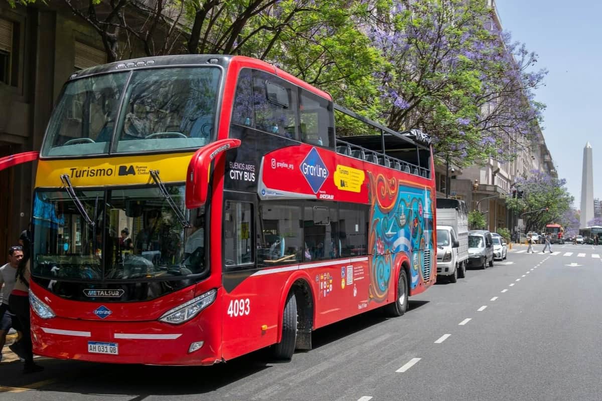 Buenos Aires : Visite guidée en bus avec arrêt Un bus touristique rouge à impériale, aux motifs colorés, stationné dans une rue bordée d'arbres et d'autres véhicules.