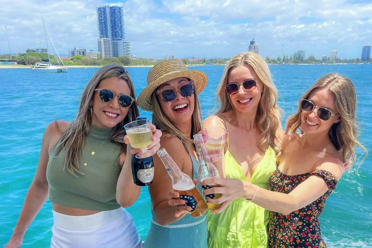 Gold Coast : Go Hopo Explorer Pass Trois femmes souriantes, un verre à la main, sur un bateau, avec en arrière-plan un front de mer pittoresque et des immeubles.