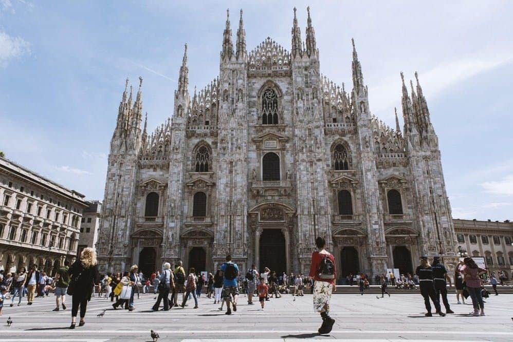 La Cène : Billet d'entrée + Visite en bus Les gens marchent et se rassemblent devant une grande cathédrale ornée de flèches pointues, sous un ciel clair.
