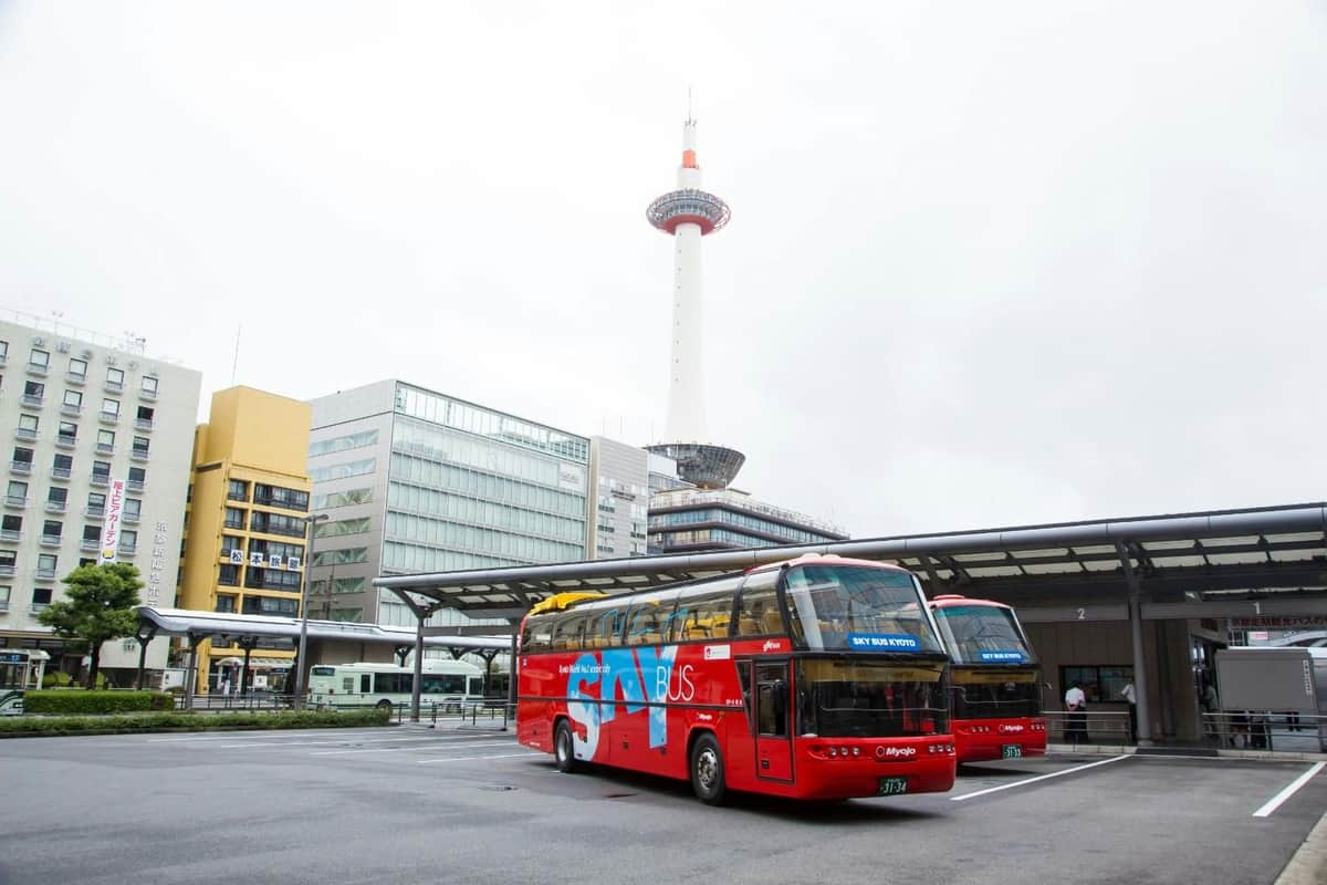 曇りの日には、近代的な建物と背の高いタワーがある駅の近くに赤い観光バスが停まっていました。