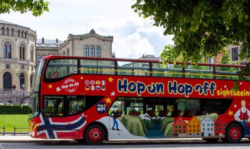 Un bus touristique à impériale d'un rouge éclatant avec le texte "Hop-on Hop-off" et divers drapeaux nationaux imprimés sur ses flancs.
