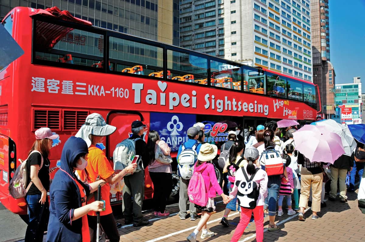 市街地で「台北観光」というラベルの付いた赤い二階建ての観光バスに並ぶ人々のグループ。