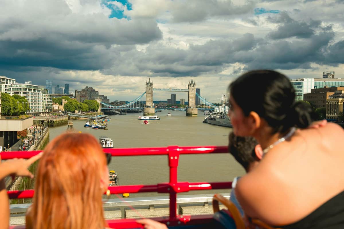 Une personne s'appuie sur une rambarde rouge, regardant vers le Tower Bridge qui enjambe la Tamise sous un ciel nuageux.