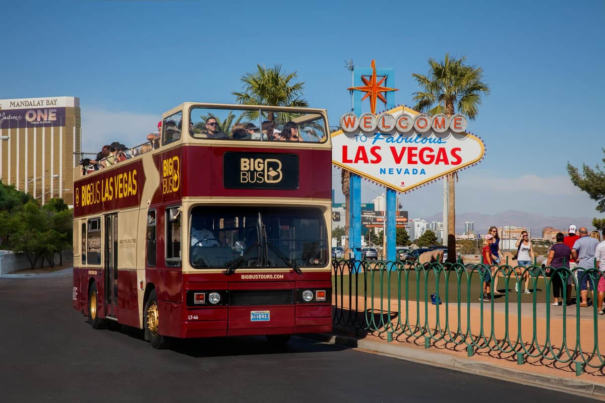 Big Bus Las Vegas : Visite en bus Hop-on Hop-off Personnes à bord d'un bus touristique à impériale devant le panneau "Welcome to Fabulous Las Vegas, Nevada", avec des palmiers en arrière-plan.