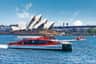 A red and white ferry labeled 'Captain Cook Cruises' on water near the Sydney Opera House and Sydney Harbour Bridge.