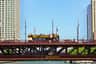A double-decker tour bus labeled "BigBus Chicago" crosses the DuSable Bridge, adorned with American flags, under a clear blue sky.